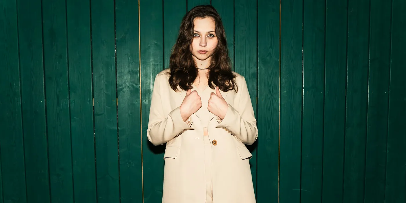 Woman in a cream tailored suit against a deep green wood-panelled wall