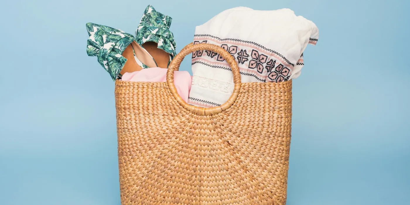 Woven straw basket bag with a printed scarf and towel on a pale blue background
