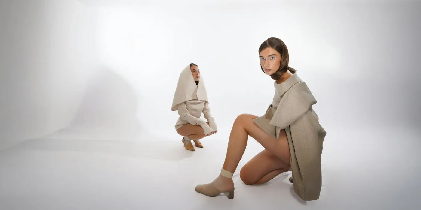 Two women in soft ivory and stone outerwear in a bright minimal studio