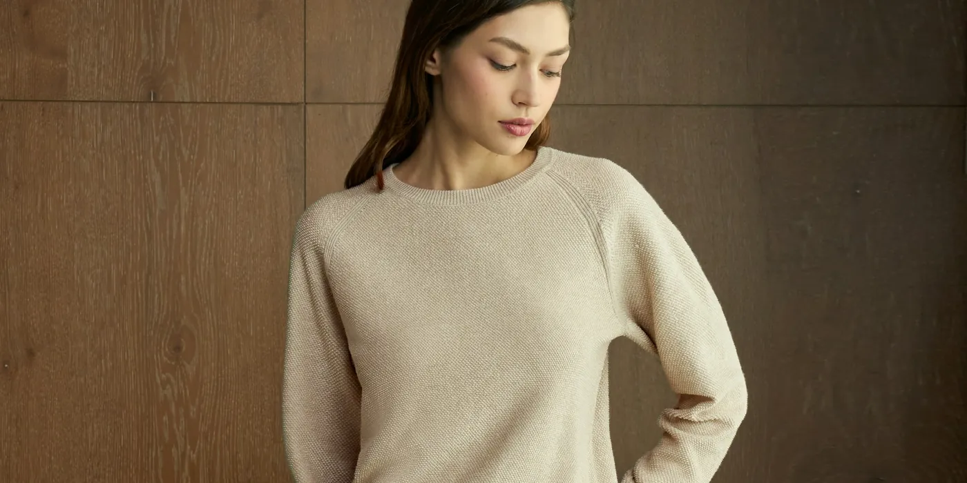 Woman in an oatmeal knit sweater against dark wood panelling