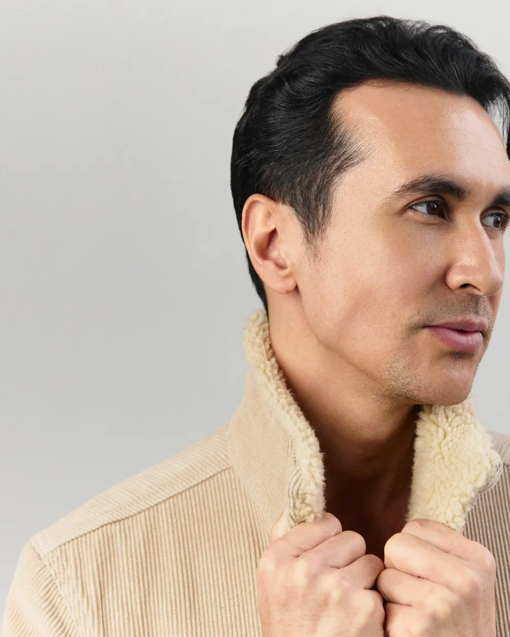 Man in a cream corduroy jacket with a shearling collar against a clean light backdrop